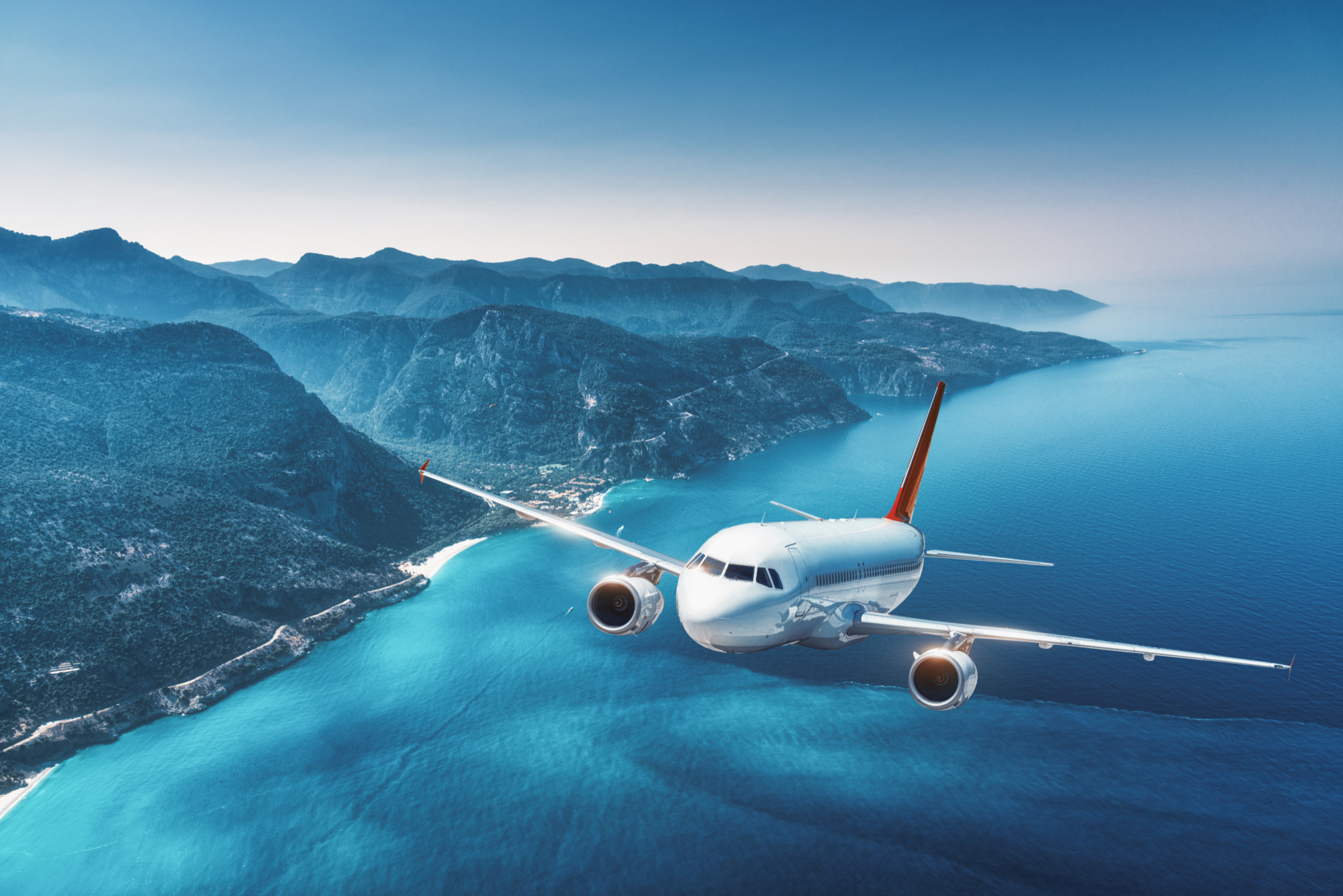 airplane flying over the ocean with an island in the background